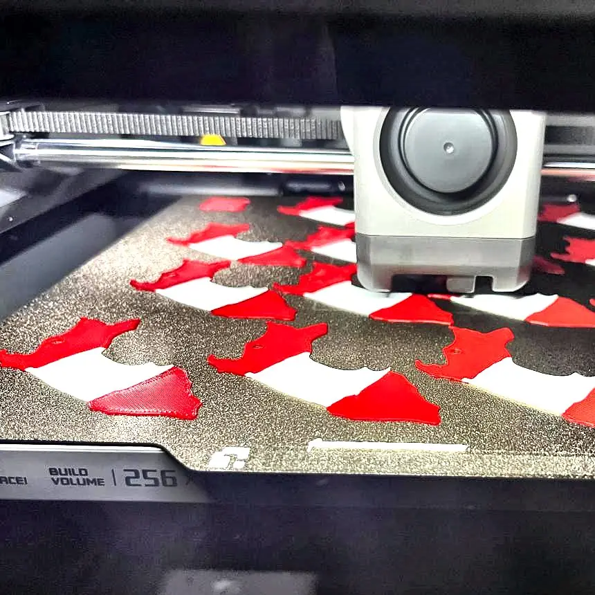 La impresora 3D del taller con la bandeja llena de piezas rojas y blancas recién impresas