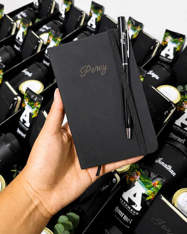 Libreta negra con lapicero grabado, sobre la mesa de armado del pedido